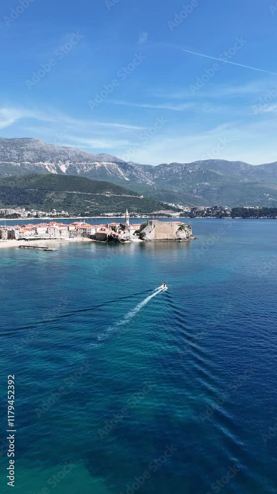 A white boat moves across the blue sea on a sunny day. A 4K aerial view of the boat captured by a drone near the old town of Budva.Vertical video A white boat moves across the blue sea on a sunny day. A 4K aerial view of the boat captured by a drone near the old town of Budva.Vertical video