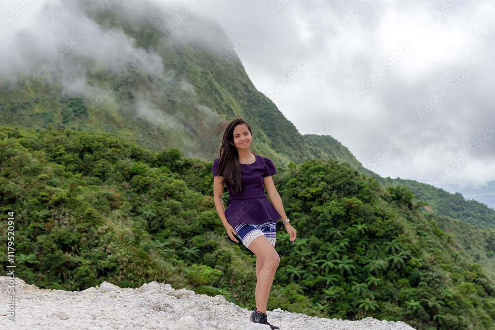 Naklejka premium Portrait of a beautiful young Filipina woman against the background of a volcano covered with smog and clouds