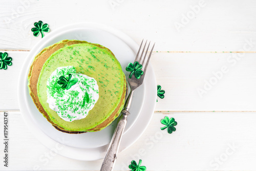 Green shamrock color pancakes with whipped cream and sugar sprinkles, for St Patrick`s day breakfast on lunch, with patricks holiday decorations on kitchen table