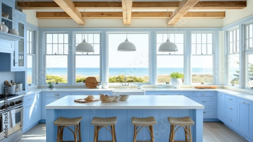 A modern coastal kitchen with light blue cabinetry, white quartz countertops, and driftwood-style bar stools. Large windows bring in natural sunlight.