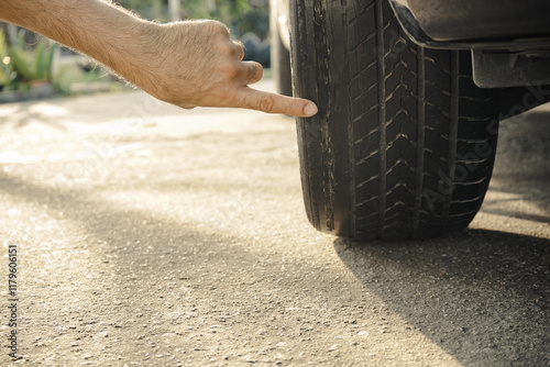 A man's hand points to a tire with bald and worn tread. Car maintenance concept.