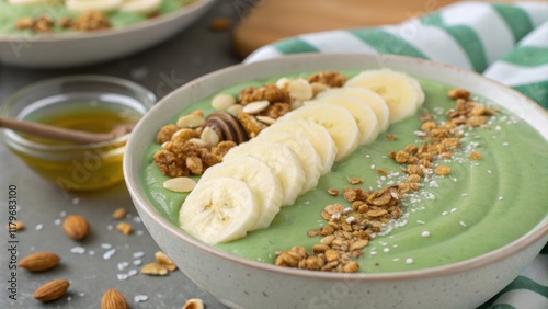 The smoothie bowls rich velvety texture is captured in a closeup its mint green surface adorned with a perfectly arranged fan of slim banana slices and crunchy granola s. A photo