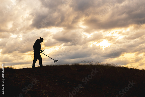 A man is walking on a hill with a metal detector in his hand
