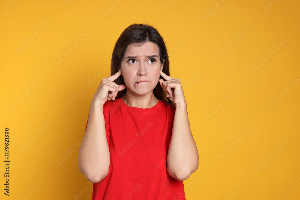 Woman covering her ears with fingers on orange background Woman covering her ears with fingers on orange background