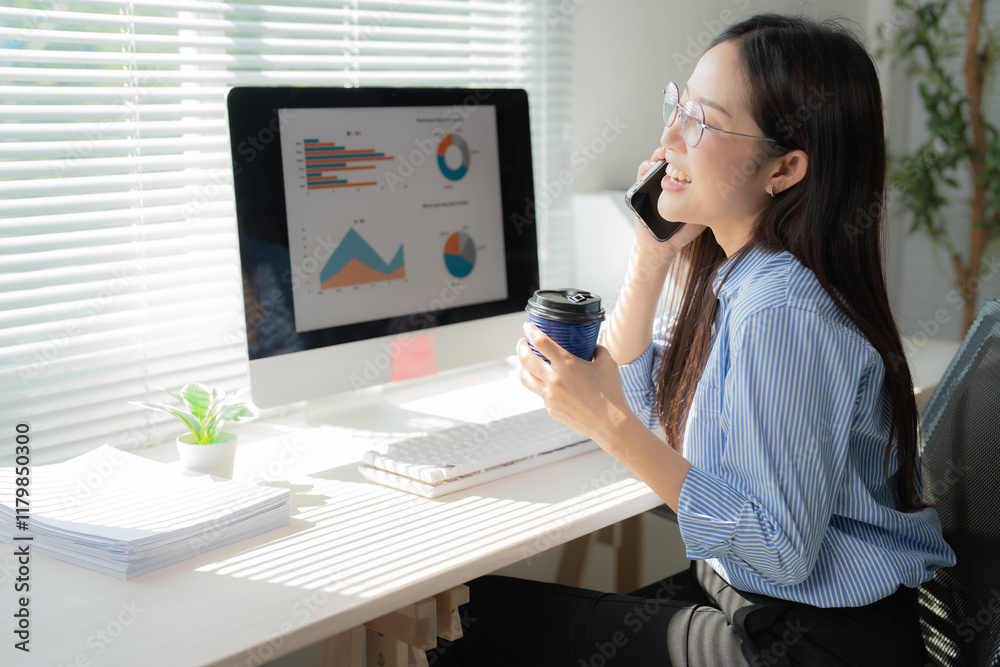 Young Asian businesswoman sipping coffee and chatting on the phone while analyzing charts and graphs on her computer in a bright, sunny office environment Young Asian businesswoman sipping coffee and chatting on the phone while analyzing charts and graphs on her computer in a bright, sunny office environment