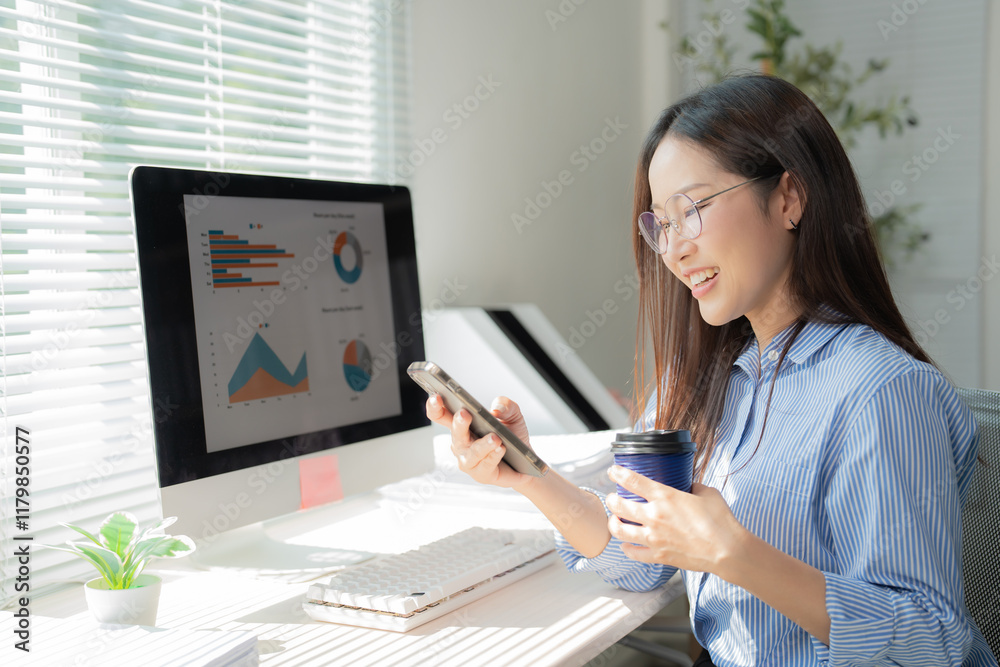 Young businesswoman analyzing financial charts displayed on computer and smartphone, drinking coffee at her desk in a bright office, enjoying work and success Young businesswoman analyzing financial charts displayed on computer and smartphone, drinking coffee at her desk in a bright office, enjoying work and success