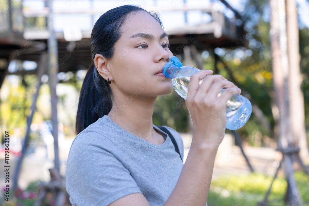 Young woman drinks clean water in a bottle After exercising to hydrate the body Standing in an outdoor green nature park, a woman is thirsty or feeling tired. Health and hydration concepts. Young woman drinks clean water in a bottle After exercising to hydrate the body Standing in an outdoor green nature park, a woman is thirsty or feeling tired. Health and hydration concepts.