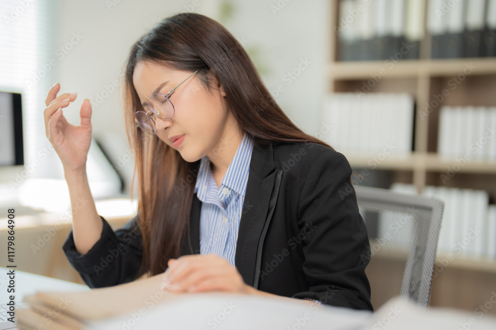 Young asian businesswoman suffering from headache, feeling tired, exhausted, having migraine symptoms after long working hours at office desk Young asian businesswoman suffering from headache, feeling tired, exhausted, having migraine symptoms after long working hours at office desk