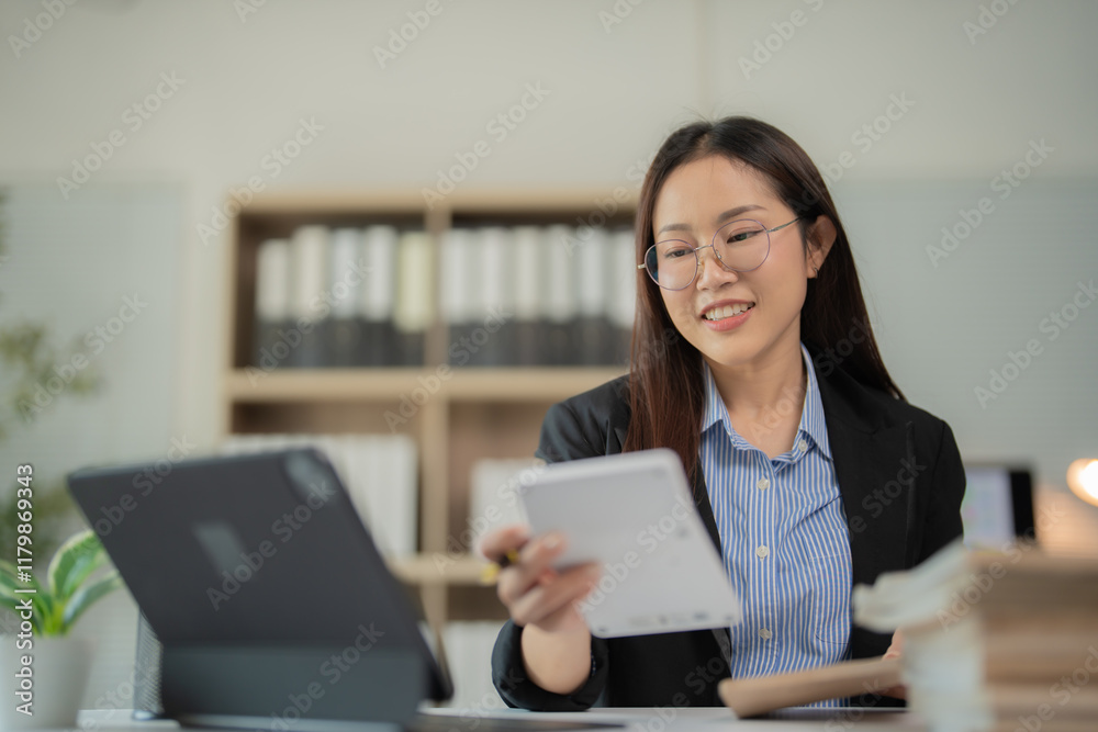 Young Asian businesswoman smiling while working on a tablet and notebook in a modern office, exuding happiness and positivity in her professional environment Young Asian businesswoman smiling while working on a tablet and notebook in a modern office, exuding happiness and positivity in her professional environment