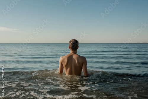 A man is in the ocean, wearing only a shirt and no pants. The water is calm and the sky is clear photo