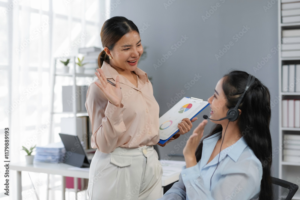 Two happy businesswomen waving during a meeting in the office while discussing graphs and pie charts Two happy businesswomen waving during a meeting in the office while discussing graphs and pie charts