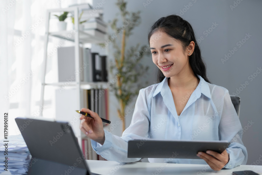 Young Asian businesswoman holding a pen and using digital tablet while working with documents in office Young Asian businesswoman holding a pen and using digital tablet while working with documents in office