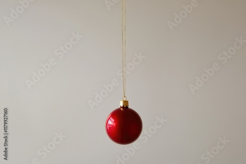 A single red Christmas ornament hangs from a gold string against a plain background.