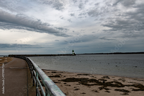 Der Weg zum Molefeuer liegt links im Bild , mit seinem Geländer aus Metall wirkt er geschwungen am  Ende der grün-weiße Leuchtturm. Recht etwas Sandstrand mit Algen und die Ostsee, ein Küstenstreifen photo