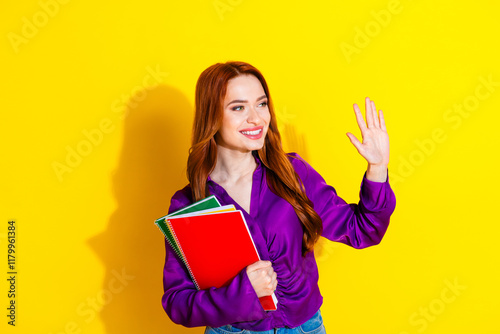 Photo portrait of lovely young lady copybooks look empty space wave hand dressed stylish violet garment isolated on yellow color background photo