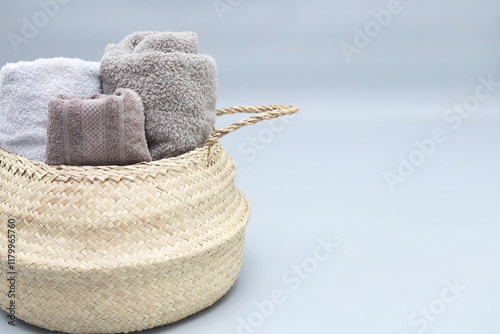 Straw wicker basket full of tolled cotton towels on grey background with copy space.