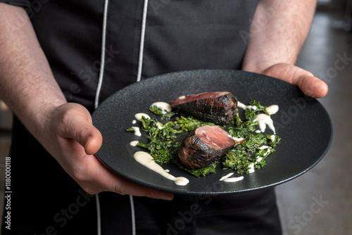 the chef is holding a plate of deer steak, with spinach. Michelin chef, luxury dishes.