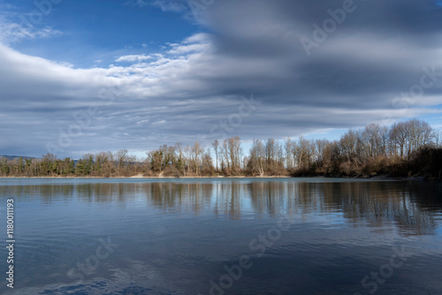 landscape on a lake with trees against clouds in alpine foehn light in autumn / fall or winter
