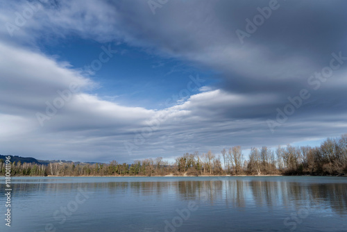 landscape on a lake with trees against clouds in alpine foehn light in autumn / fall or winter
