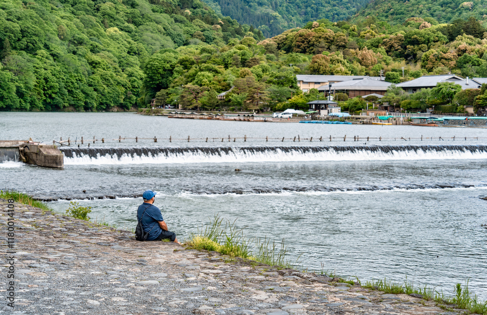Obraz premium Single unidentifiable man sitting on the bank of Katsura river in Arashiyama district, Kyoto.
