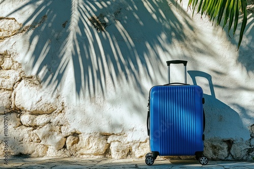 Blue suitcase rests against tropical wall, palm shadow