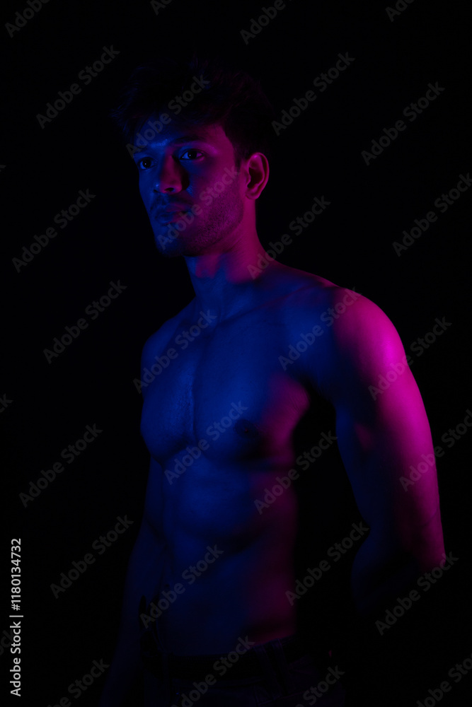 Naklejka premium Junger Mann aus Indien steht mit freiem Oberkörper in buntem Licht und posiert