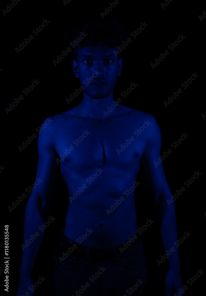 Naklejka premium Junger Mann aus Indien steht mit freiem Oberkörper in buntem Licht und posiert