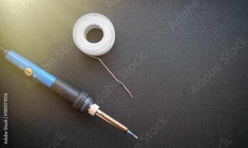 An electric soldering iron with a metal tip and a coil of wire on a dark background. Soldering of wires and microchips.Electronics repair. photo