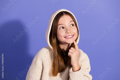Smiling young girl in a cozy hoodie posing against a purple background, conveying happiness and curiosity. photo