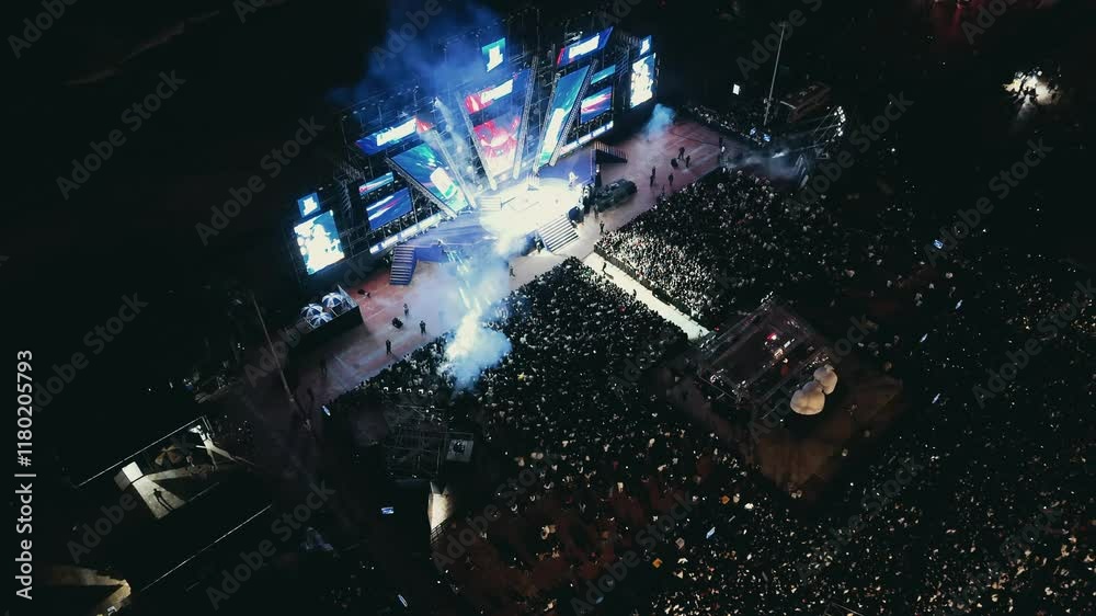 Open air music concert festival. Massive crowd gathering for night event near coastline. Colorful stage lighting illuminating energetic music performance with dynamic visual effects