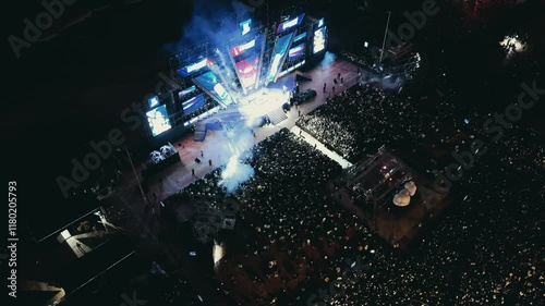 Open air music concert festival. Massive crowd gathering for night event near coastline. Colorful stage lighting illuminating energetic music performance with dynamic visual effects