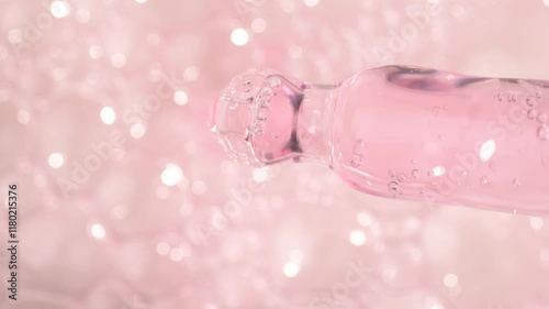 Essential oil drop dripping from pipette dropper on a pink blured background, macro.