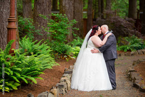 Bride and groom standing in a garden embracing and kissing photo