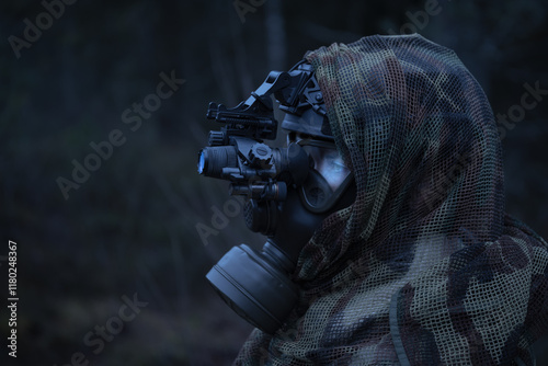 A soldier woman in a gas mask and a helmet with a night vision device in the forest at dusk. Side view. photo