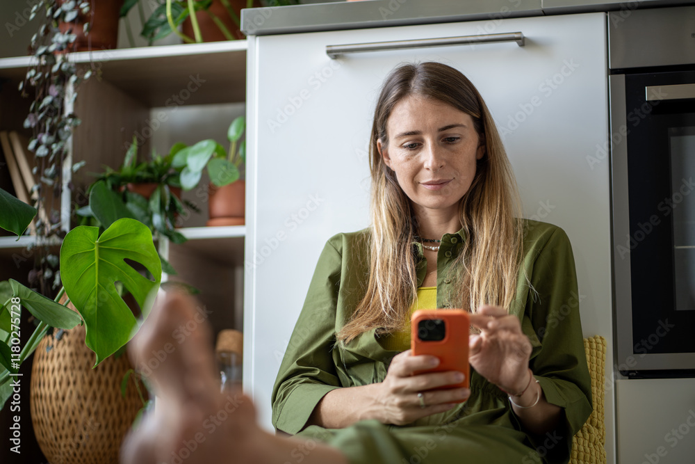 Joyful woman captures moment on smartphone on pause from chores, sit on floor in kitchen, surrounded by plants. Home environment, daily life, digital routine, plant lover, web feed addition at home Joyful woman captures moment on smartphone on pause from chores, sit on floor in kitchen, surrounded by plants. Home environment, daily life, digital routine, plant lover, web feed addition at home