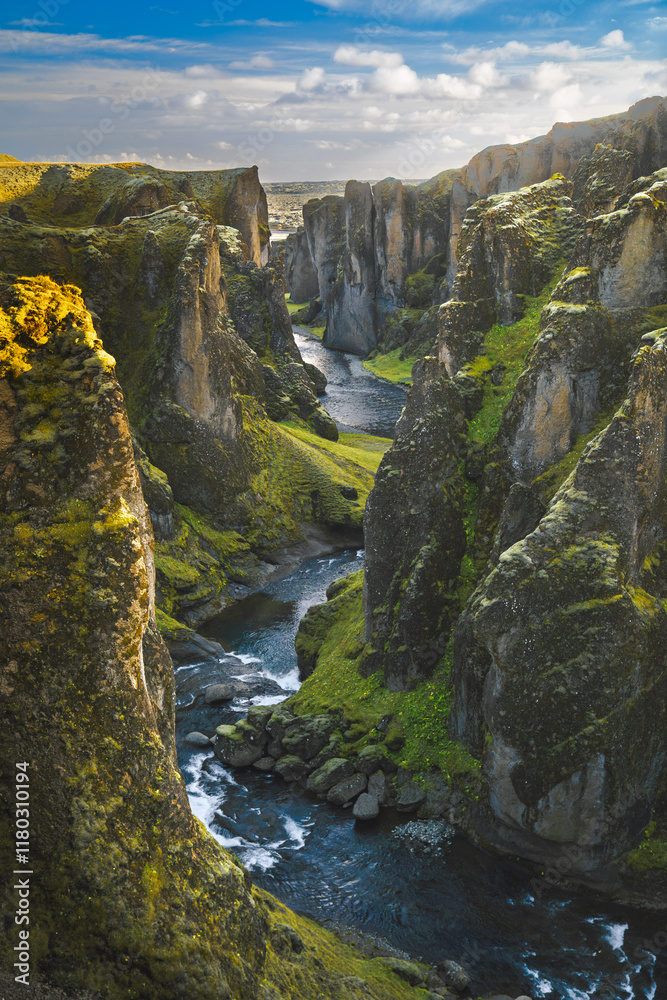 Obraz premium A breathtaking view of Fjaðrárgljúfur Canyon with a winding river, moss-covered cliffs, and vibrant vegetation.