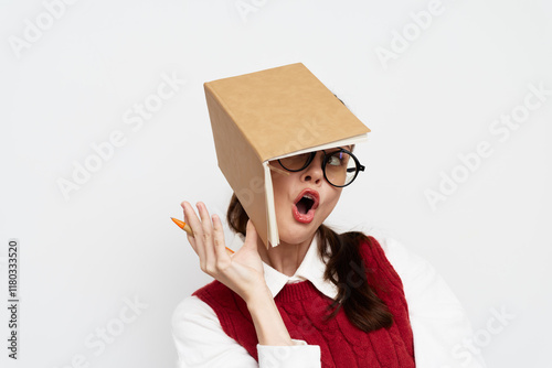 Humorous woman with a book on her head showing surprise, wearing glasses and a red sweater, against a plain white background, expressing a playful and creative concept photo