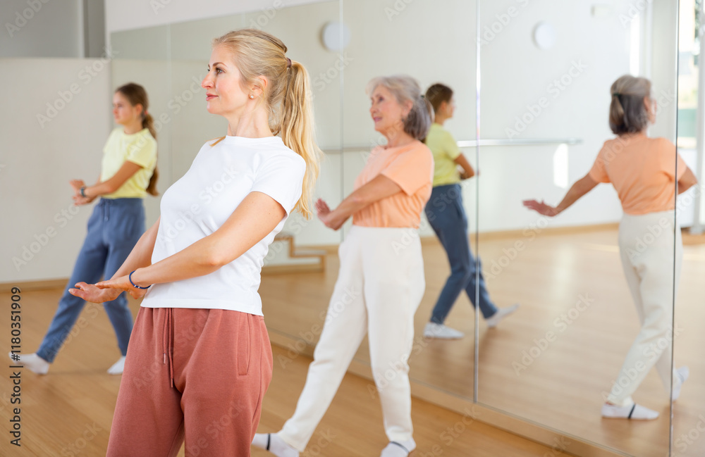 Naklejka premium Middle aged adult athletic blonde woman dancing during group class in dance center