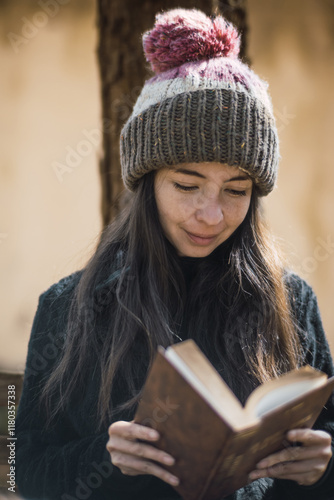Beautiful white girl with oriental features reading a book in the park, sitting on a bench with the sunset light coming through the branches.