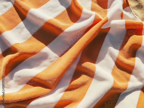 A vibrant close-up of an orange and white striped beach towel, softly folded under warm summer sunlight photo