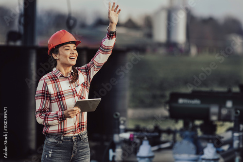 Female engineer with waving hand in front of irrigation plant in agricultural field. photo