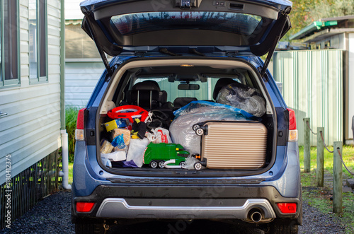 A family SUV is packed to the brim for a road trip, overflowing with cluttered luggage, toys, and camping gear, ready for an exciting adventure. The trunk is loaded with a miscellany of items