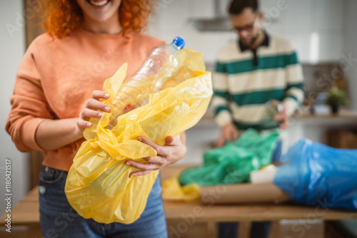 Obraz na plátně Woman throwing empty plastic bottle in yellow garbage bag at home