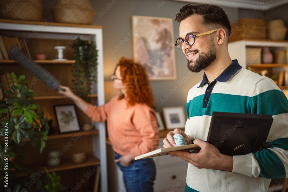 Fototapeta premium boyfriend dusting photo frame while girlfriend clean behind him