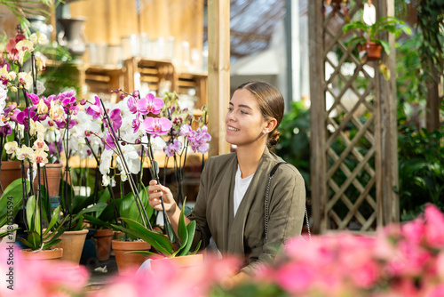 Young woman lovingly selects a flower pot with orchid flowers in a flower shop photo