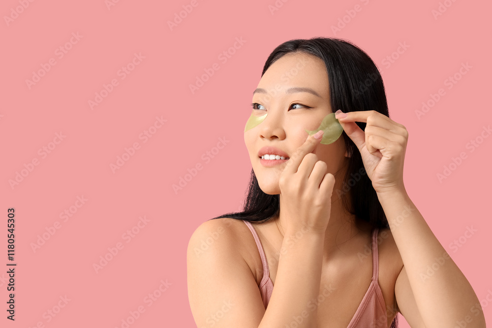 Young Asian woman applying under-eye patches on pink background, closeup Young Asian woman applying under-eye patches on pink background, closeup