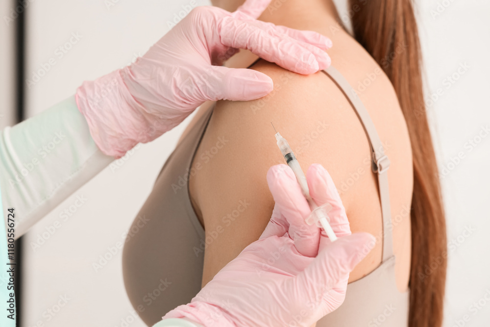 Fototapeta premium Young woman receiving injection in her shoulder at cosmetologist's office, closeup