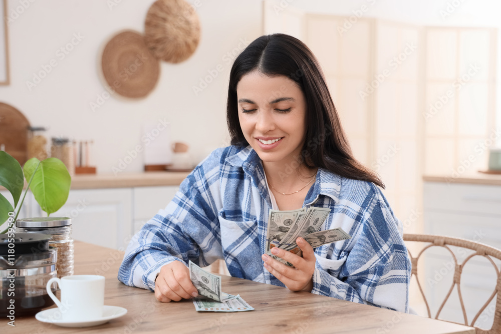 Beautiful woman counting dollar banknotes at table in kitchen Beautiful woman counting dollar banknotes at table in kitchen