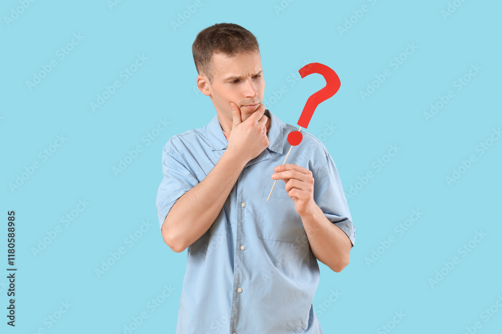 Thoughtful young man with paper question mark on blue background Thoughtful young man with paper question mark on blue background