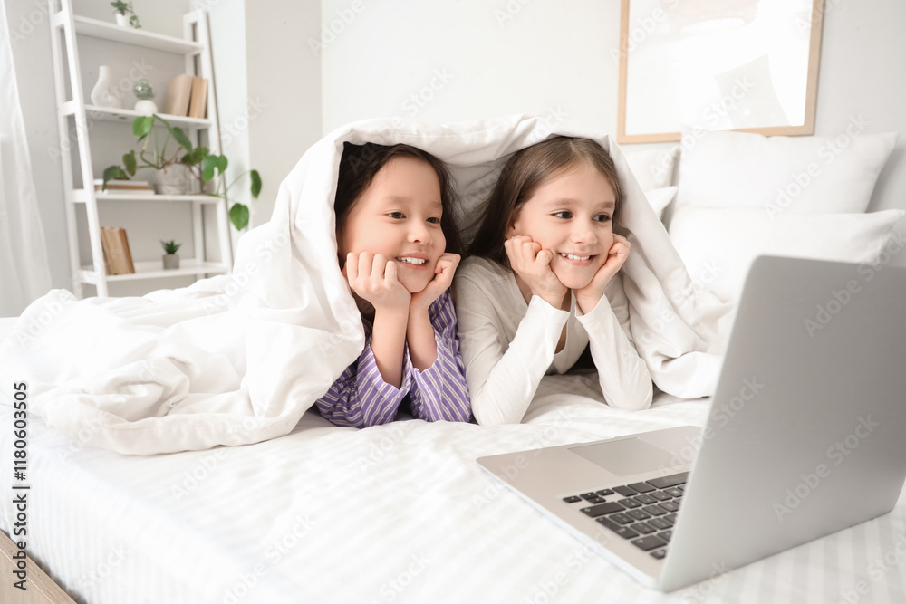 Cute girls under blanket watching cartoons on laptop in bedroom Cute girls under blanket watching cartoons on laptop in bedroom